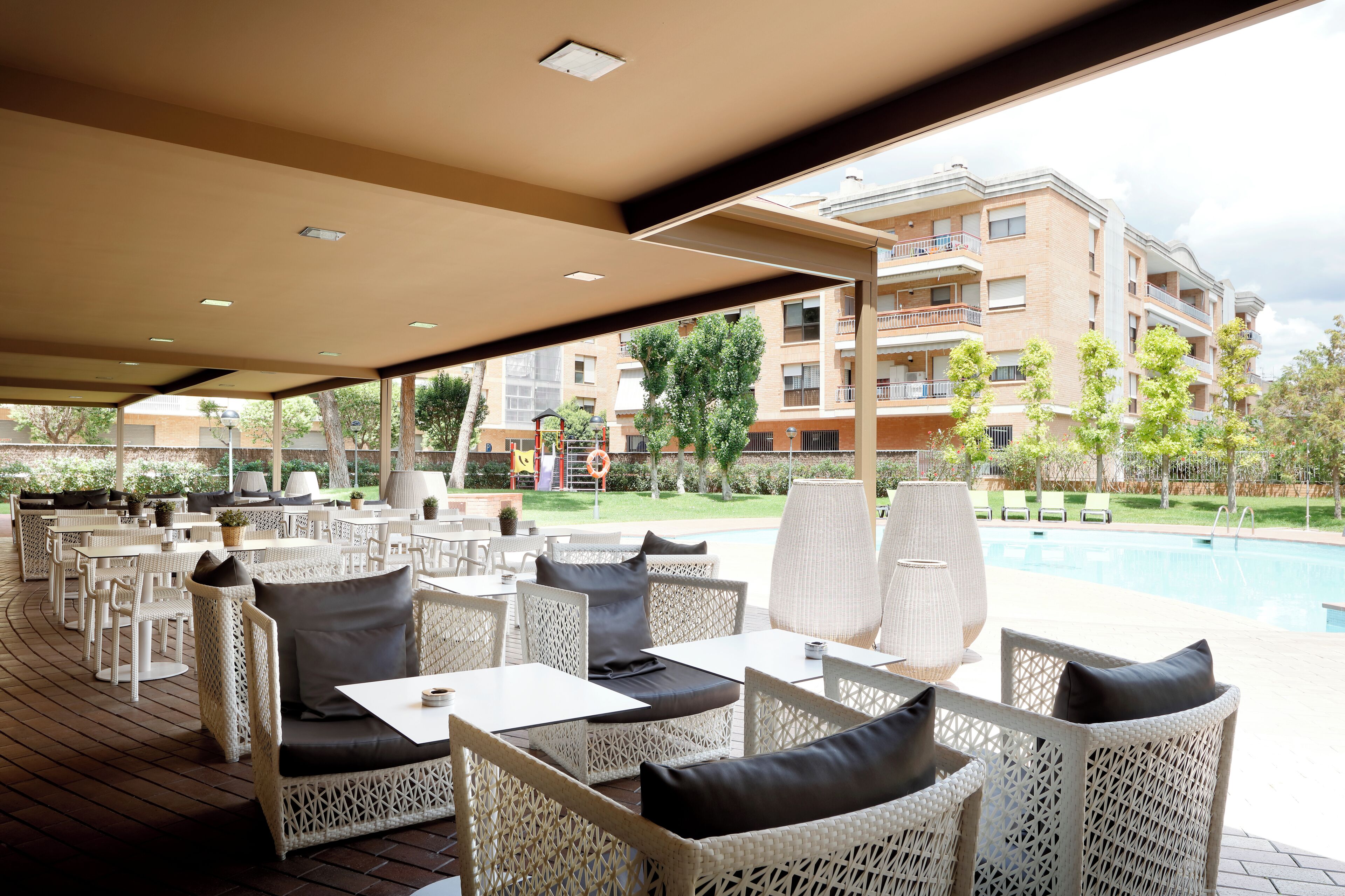 An outdoor patio area with wicker furniture, a pool, and a building in the background.