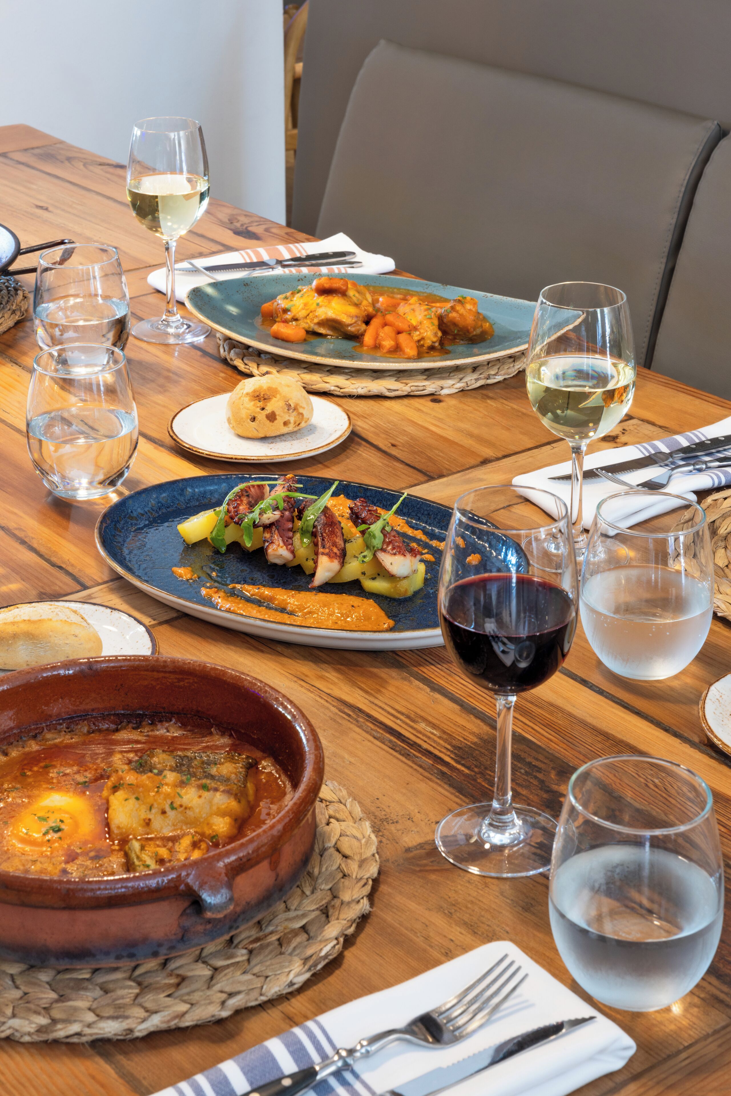 A wooden dining table with plates of food, glasses of wine, and cutlery.