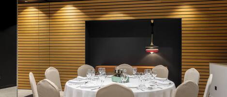 Un salón de conferencias con mesas redondas, manteles blancos y sillas color beige.