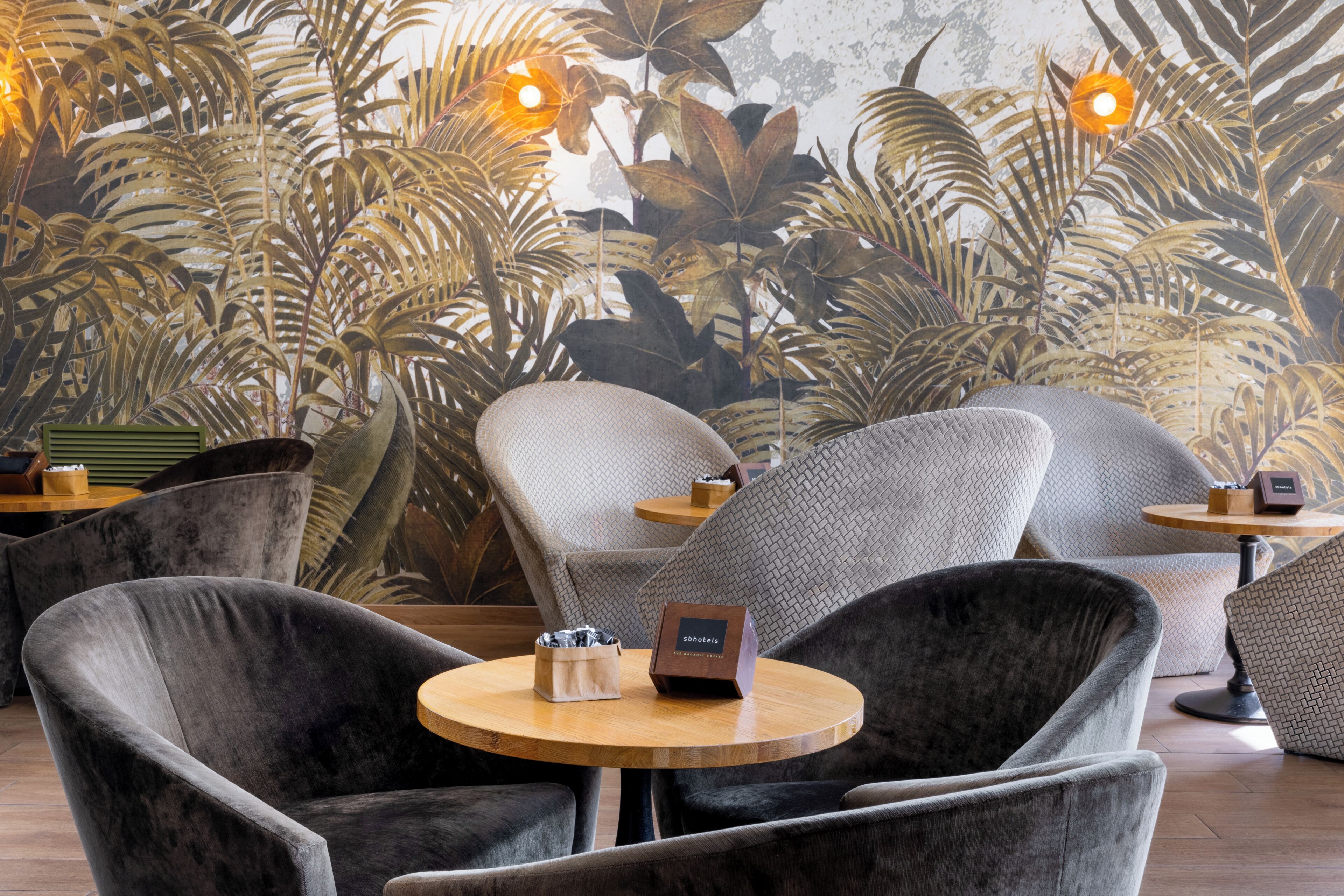 A seating area with round tables, cushioned chairs, and a wall with large tropical leaves.