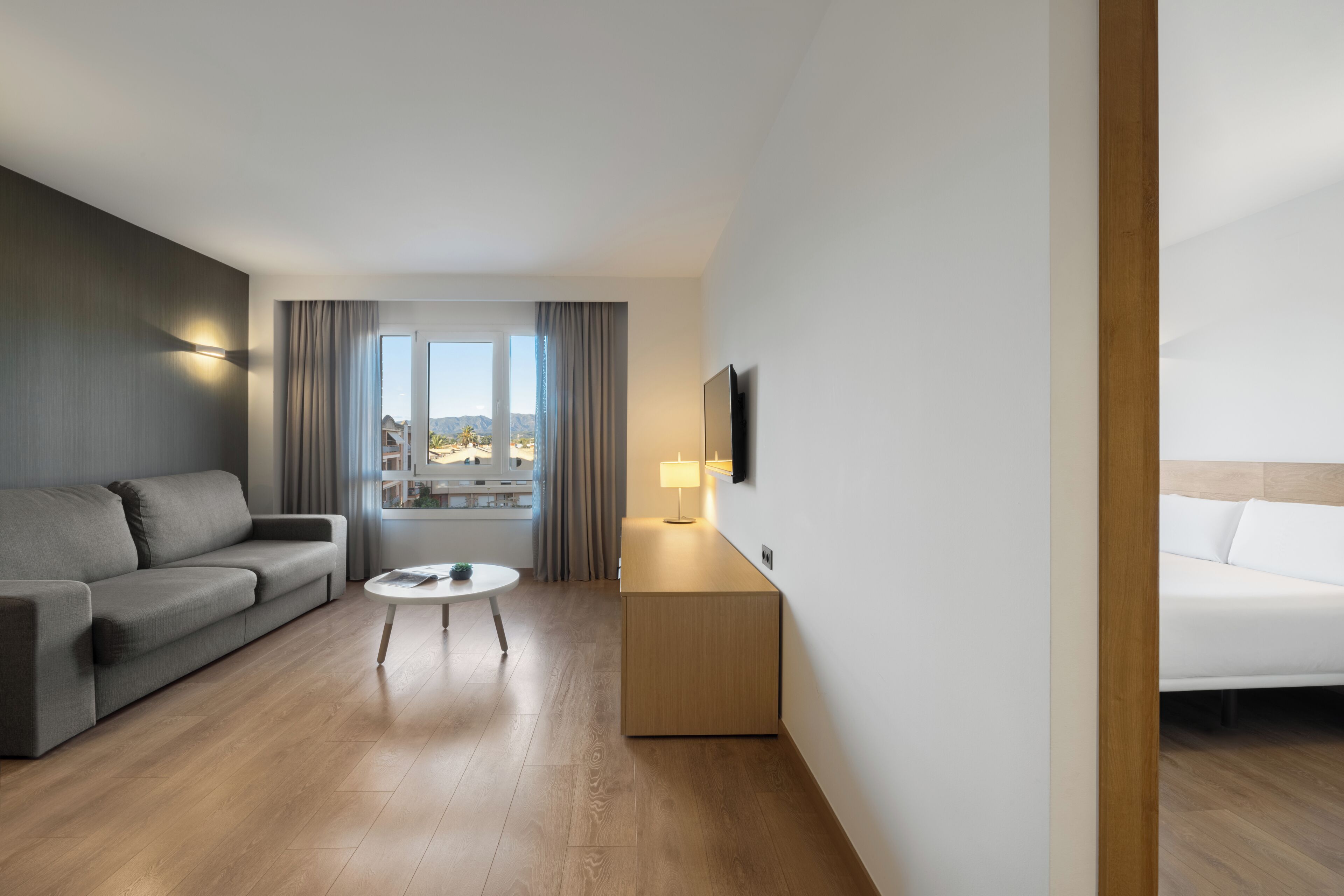 A hotel room with a sofa, a small table, a TV, and a bed.