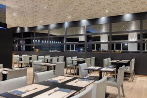 Een restaurant met meerdere tafels en stoelen, grote ramen en een modern plafondontwerp.