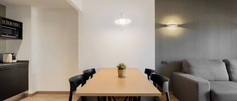 Un comedor moderno con una mesa de madera, sillas negras, una planta en maceta y un sofá gris.