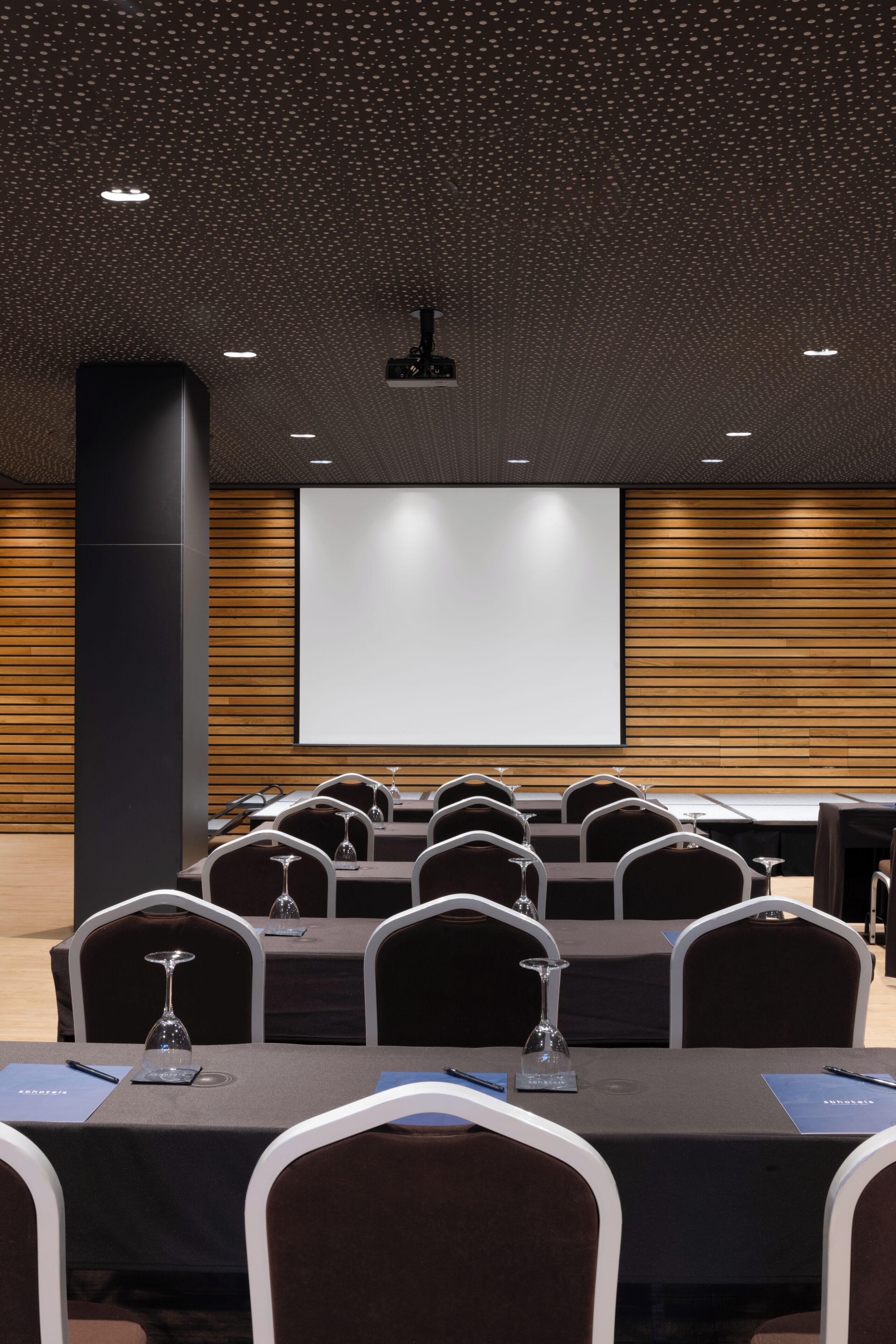 A conference room with a large screen, multiple tables with chairs, and a projector.