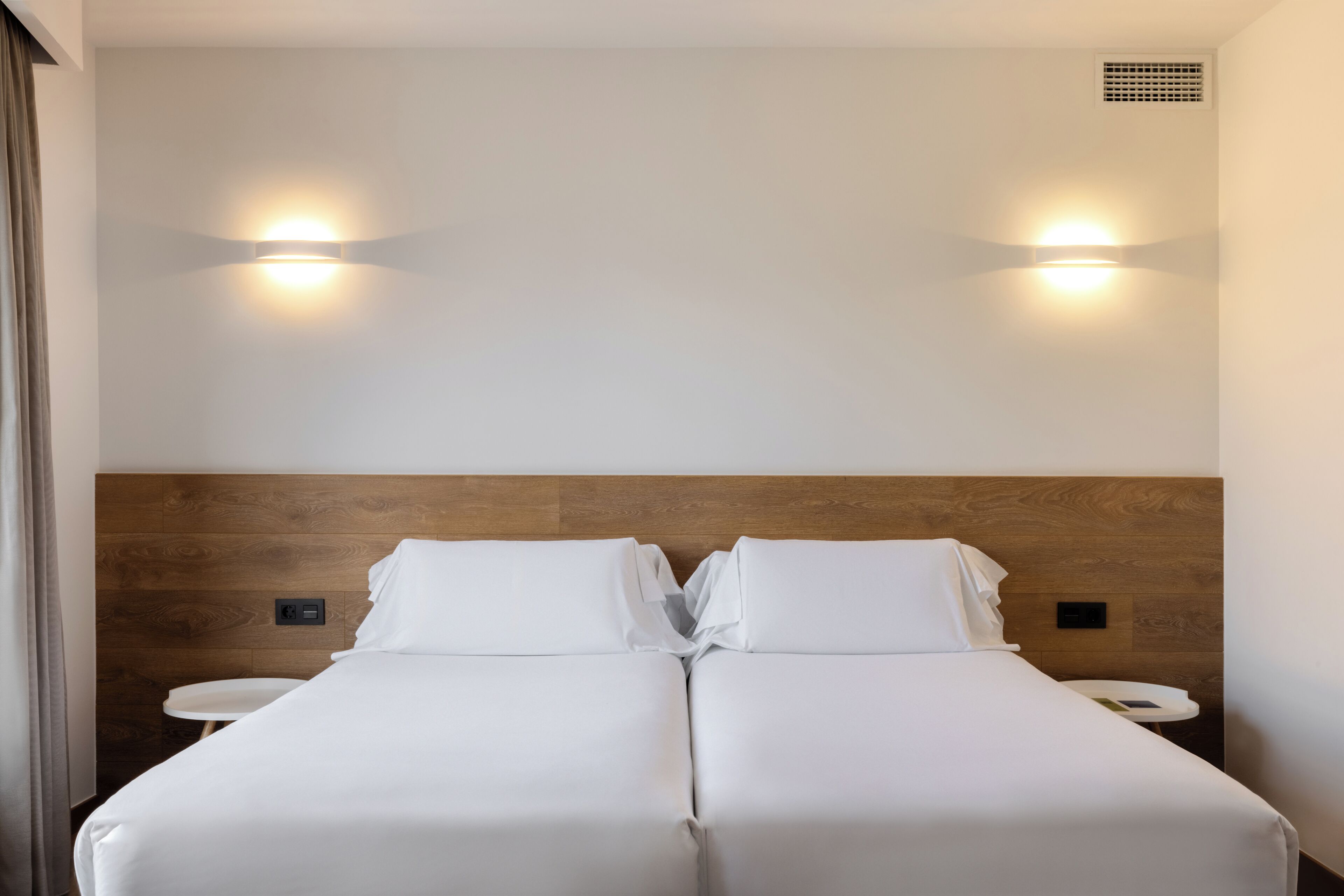 Una cama doble con cabecera de madera, dos mesitas de noche y luces fijadas a la pared.