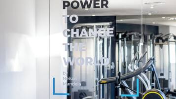 Un gimnasio con equipo de ejercicio, una frase motivacional en la pared y el reflejo del equipo en la pared de vidrio.