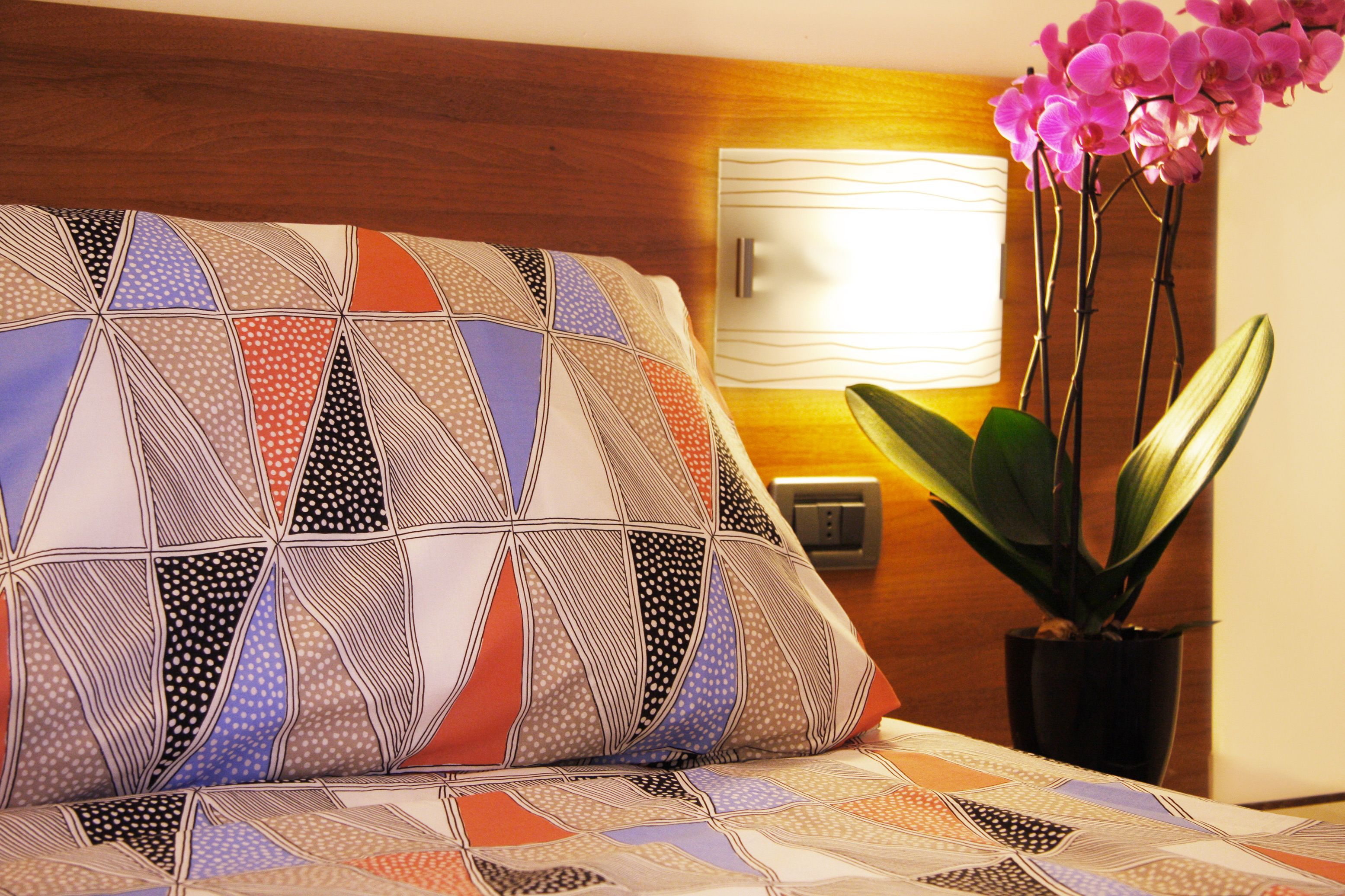 A hotel room with a patterned bedspread, a bedside lamp, and a potted plant.