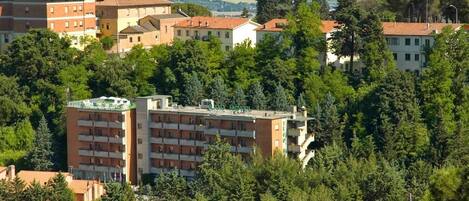 A multi-story building with a flat roof, surrounded by dense greenery and other residential buildings.