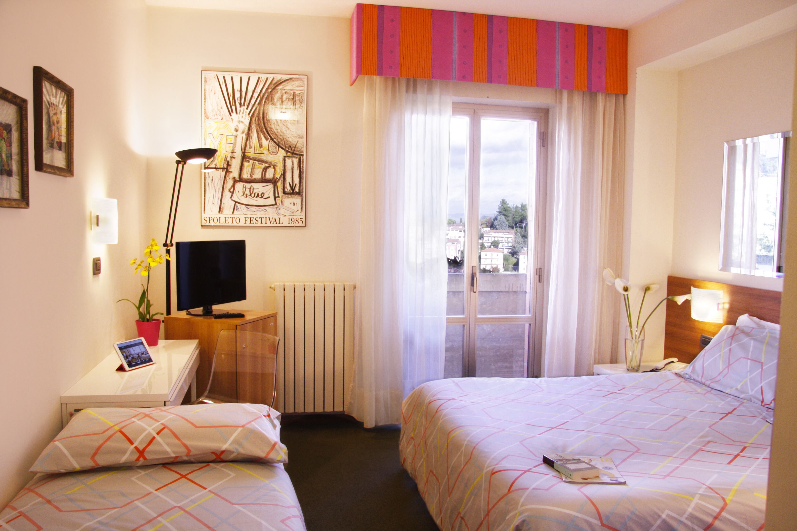 Une chambre d’hôtel avec deux lits, un bureau avec un ordinateur, une télévision et une fenêtre donnant sur des immeubles.