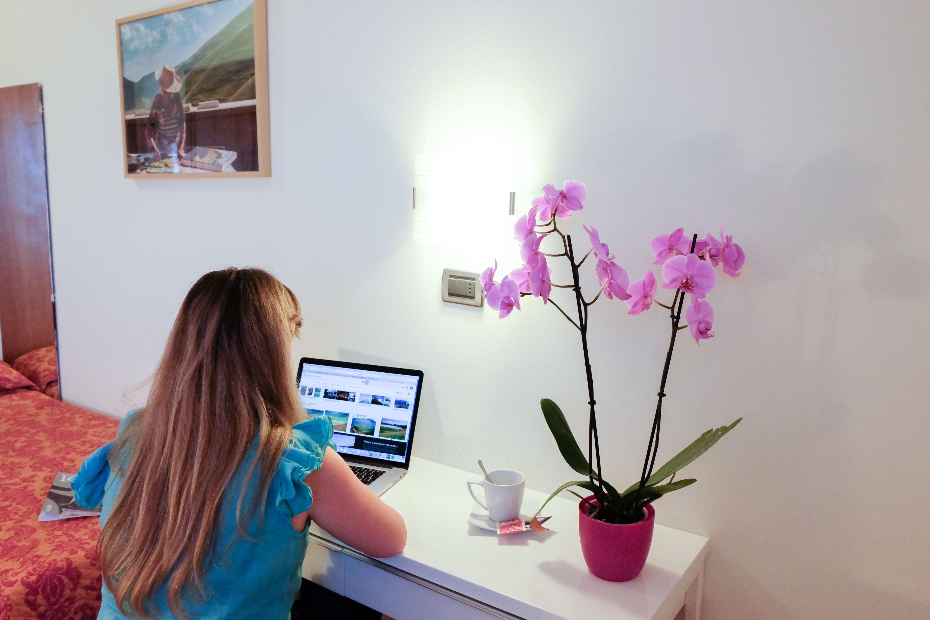 Una persona che usa un portatile a una scrivania con un'orchidea rosa e una tazza bianca.