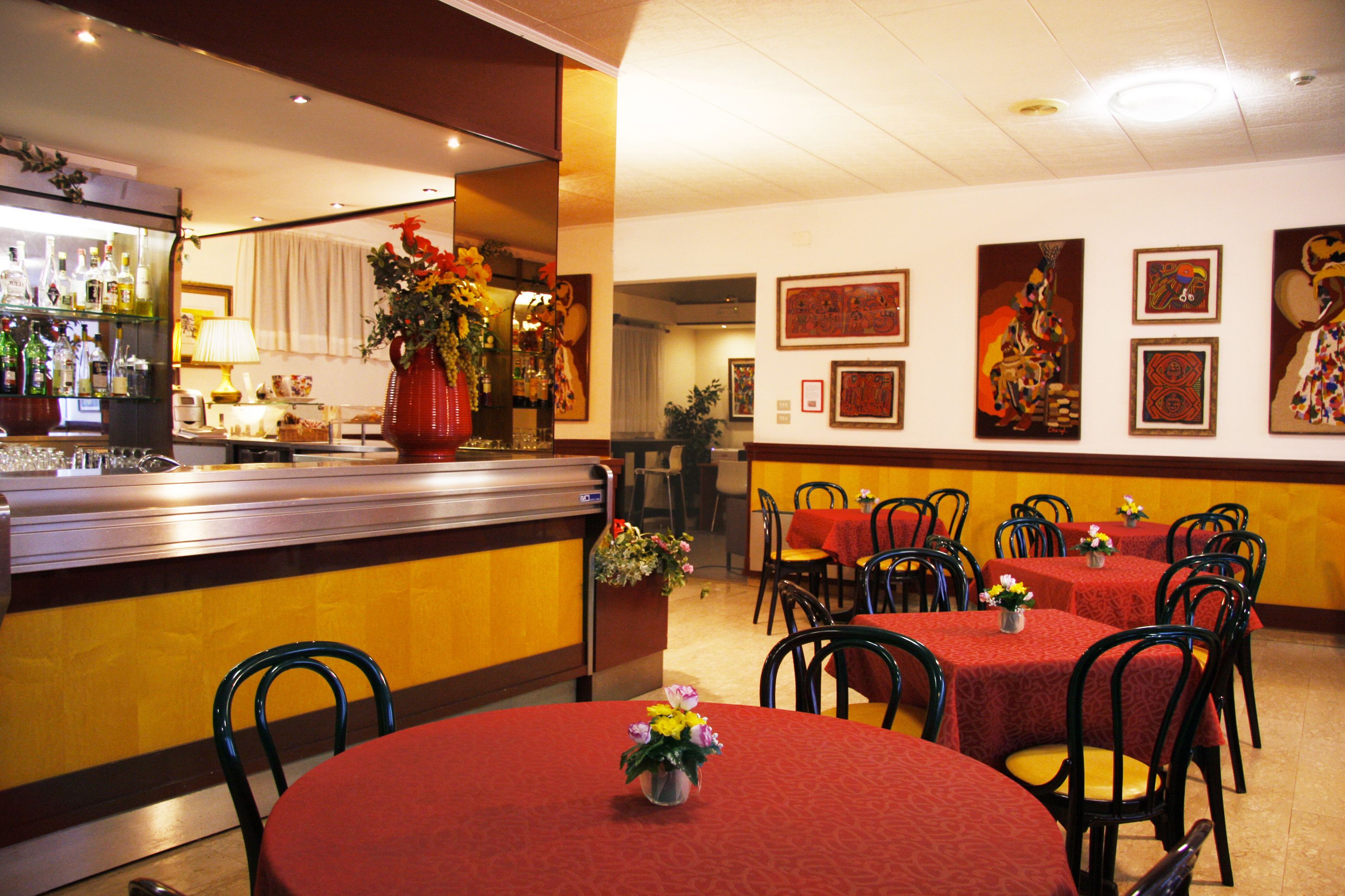 Un restaurante con manteles rojos, sillas negras y una zona de bar con botellas y vasos.