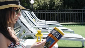 A person reading a book titled "Umbria" by a pool with white lounge chairs and a yellow lantern. - Hotel Ilgo (Perugia)