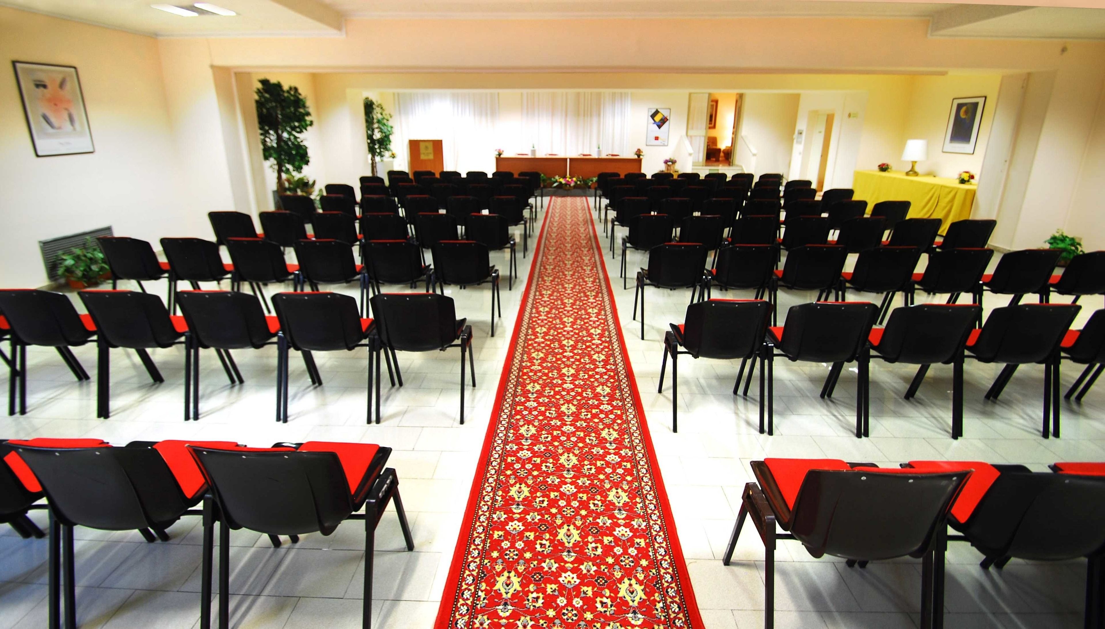 A conference room with rows of black chairs and a red carpet leading to a podium.