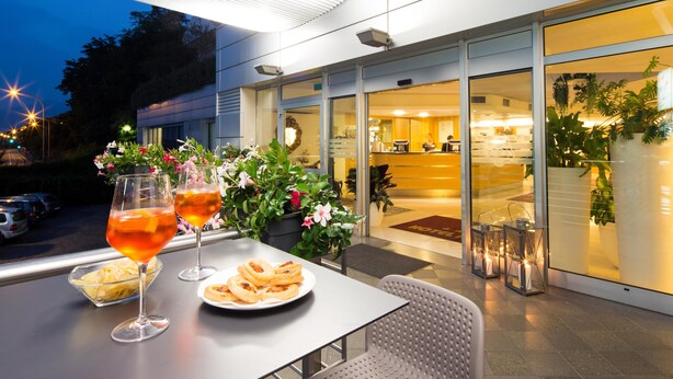 An outdoor dining area with a table set for two, featuring a plate of pastries and two glasses of a red beverage. - Best Western Hotel Adige (Trento)