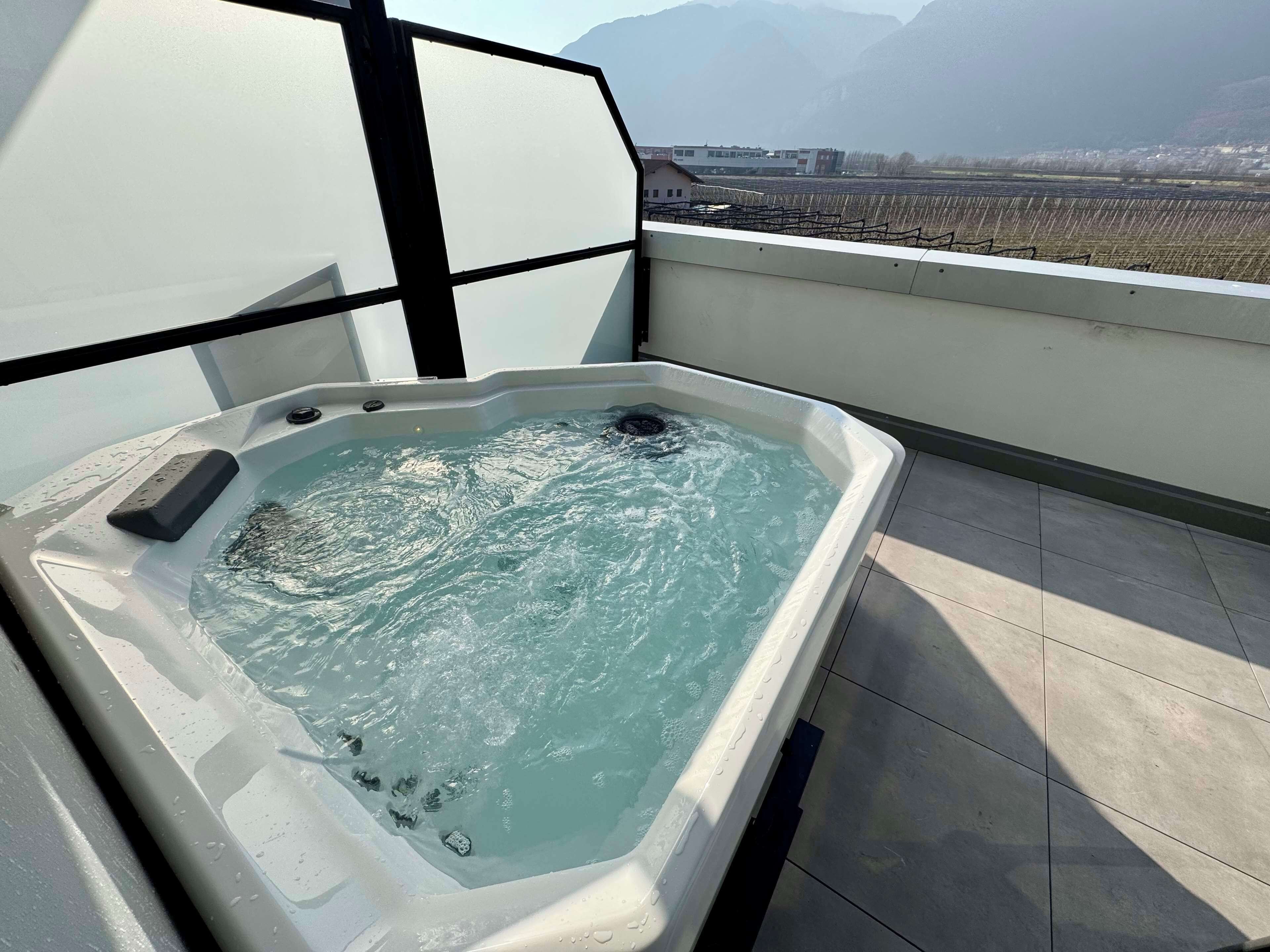 A hot tub on a balcony with a view of a vineyard and mountains in the background.