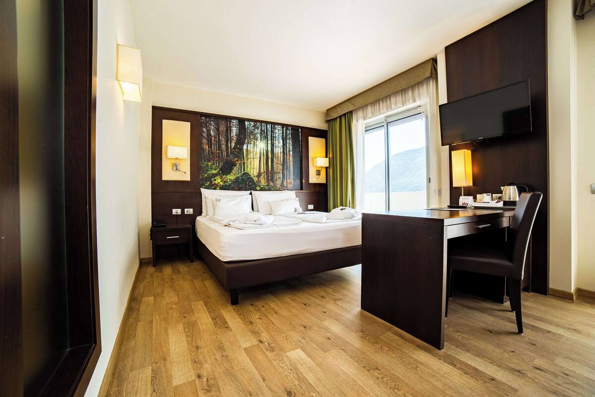A hotel room with a bed, desk, and a large window.