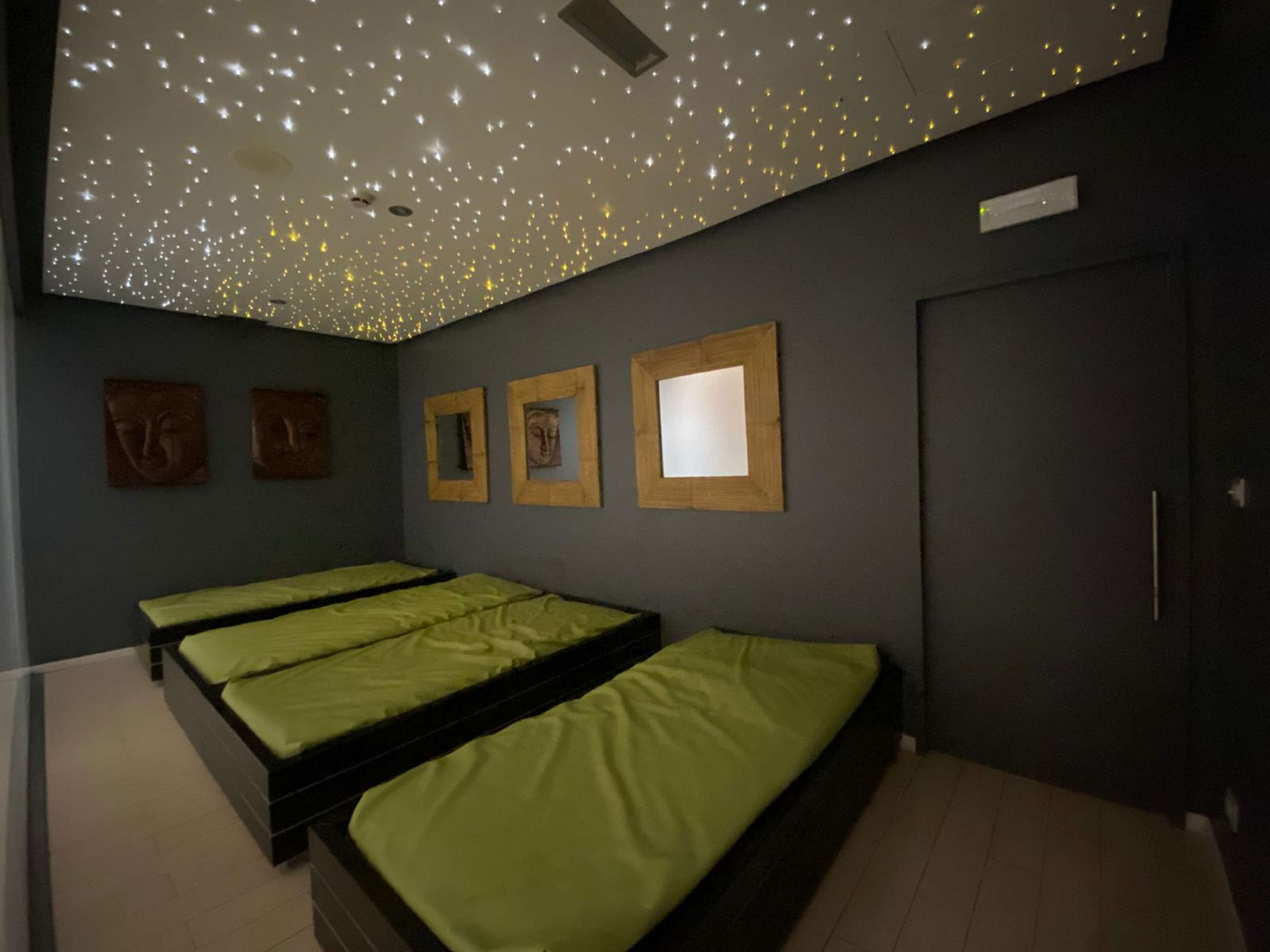A room with three beds, a ceiling with star-like lights, and three framed pictures on the wall.