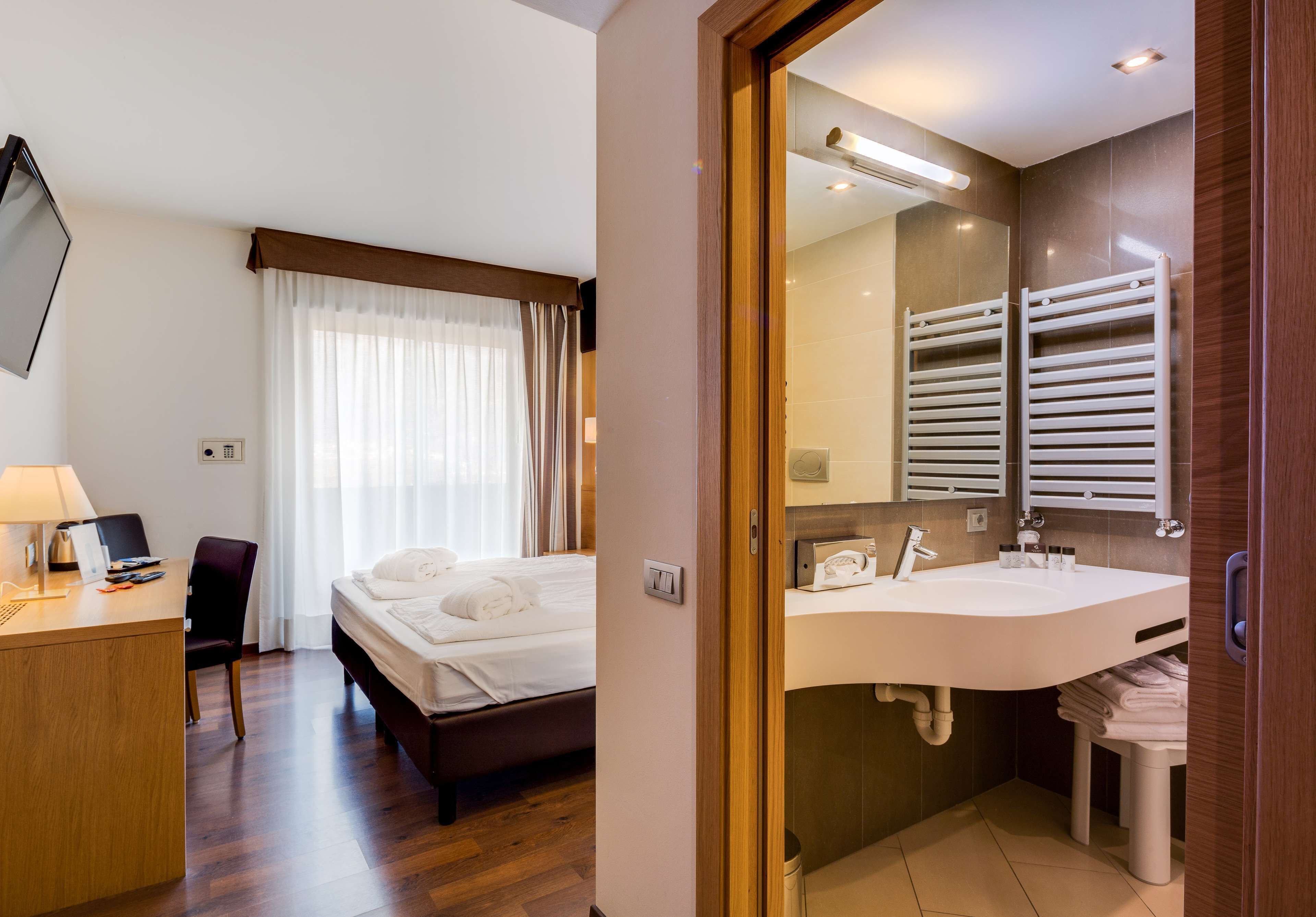 A hotel room with a bed, desk, chair, and a bathroom with a sink and towel rack.
