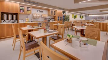 Un espace repas moderne avec des tables et des chaises en bois, un coin cuisine équipé d’appareils électroménagers en acier inoxydable, et un mur orné d’une enseigne « CUSNC ».