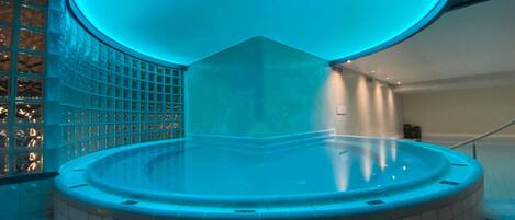 A modern indoor swimming pool with a blue-lit ceiling, tiled walls, and a curved design.