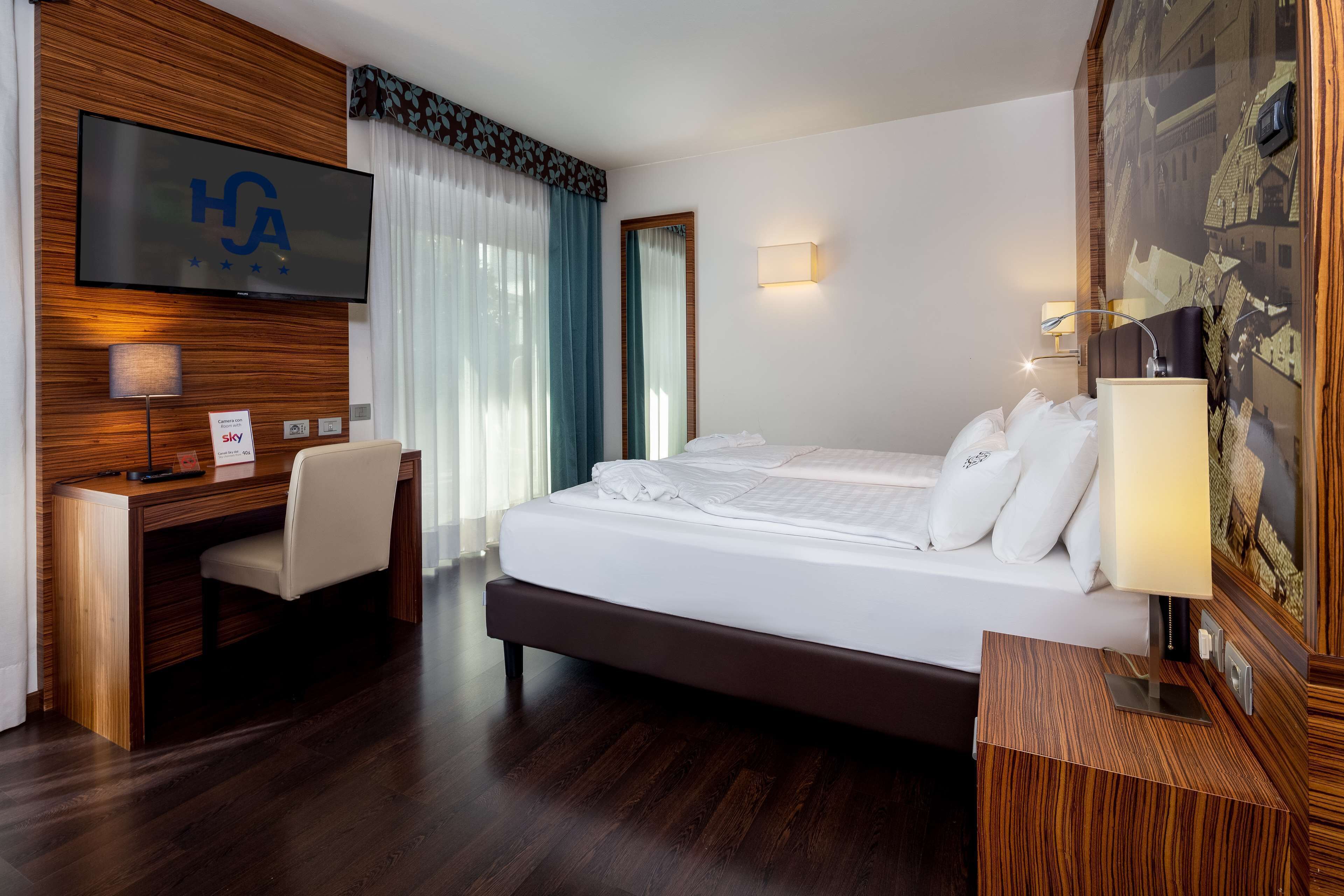 Una habitación de hotel con una cama grande, un escritorio, un televisor montado en la pared y un mural con vistas a la ciudad.