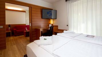 A hotel room with two beds, a desk, a chair, a red sofa, a TV, and a window with curtains.