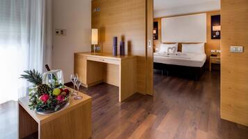 A hotel room with a wooden desk, a bed with white bedding, a nightstand, and a wall-mounted lamp.