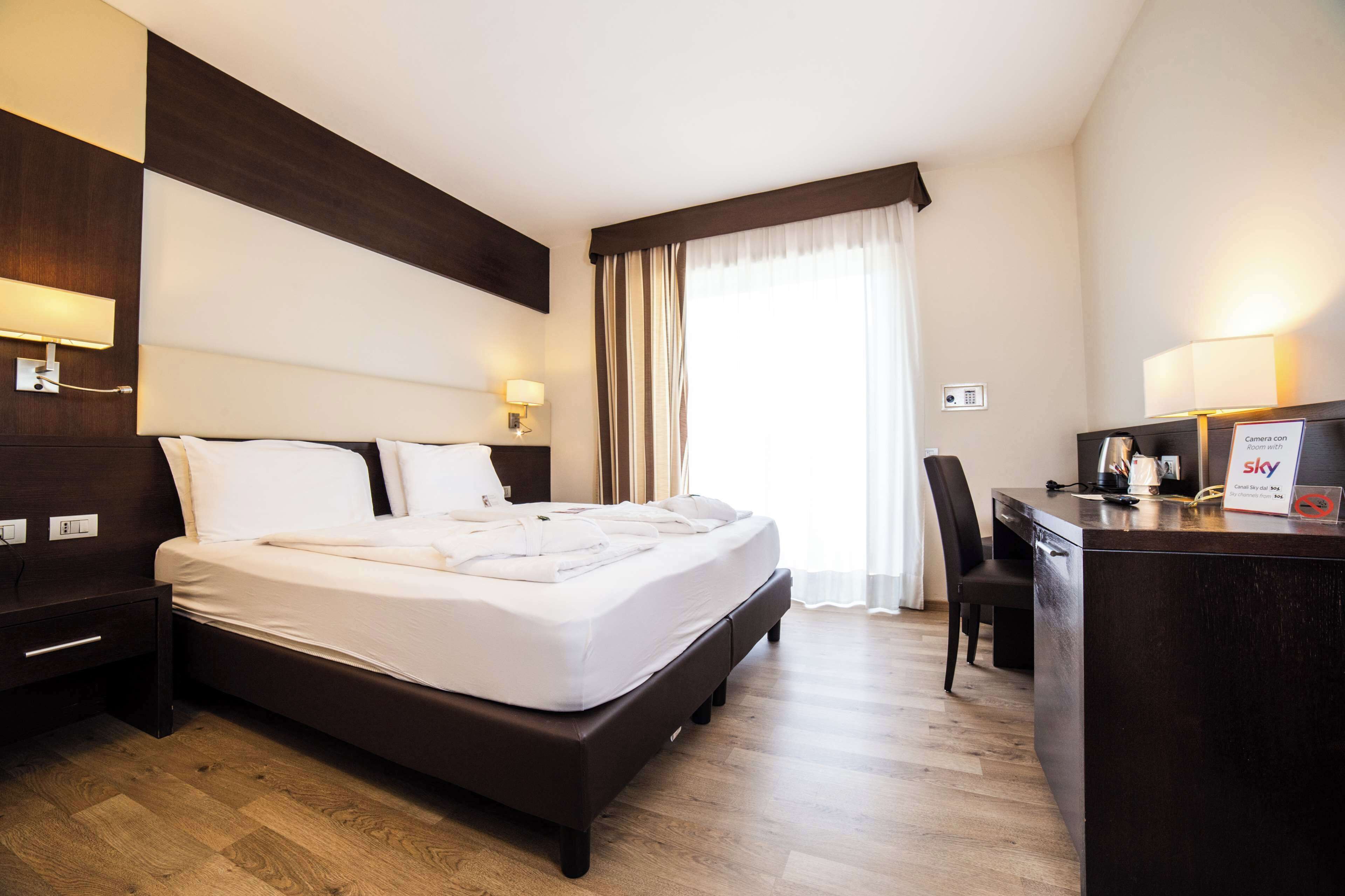 A hotel room with a large bed, a desk with a computer, and a window with curtains.