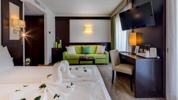 A hotel room with a large bed, a desk, a television, and a green sofa.