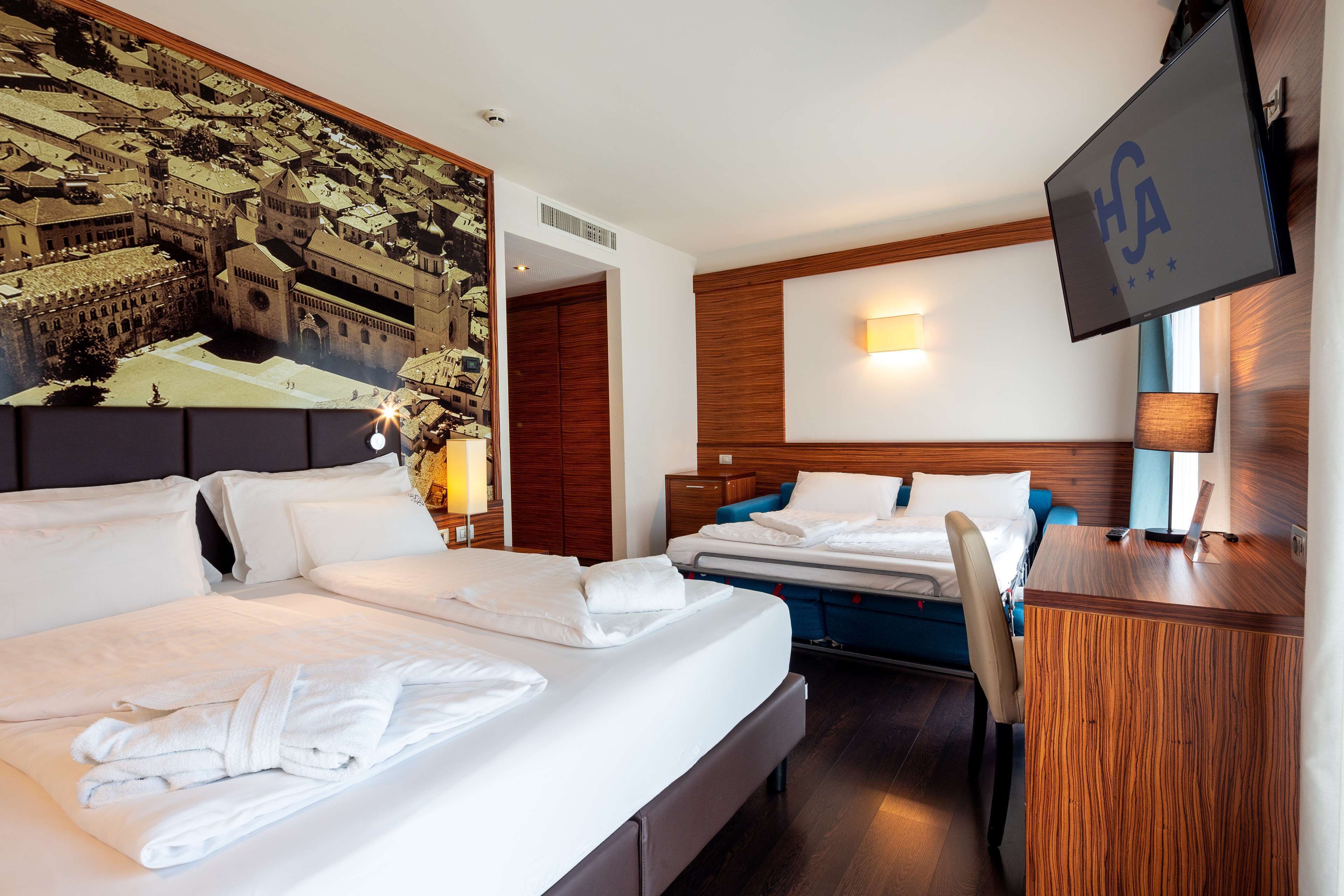 A hotel room with two beds, a desk, a TV, and a mural of a cityscape.