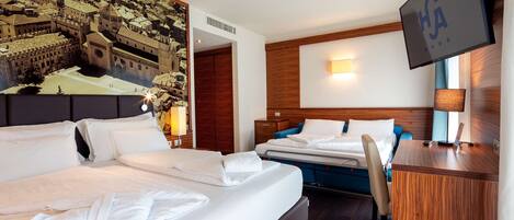 A hotel room with two beds, a desk, a TV, and a mural of a cityscape.