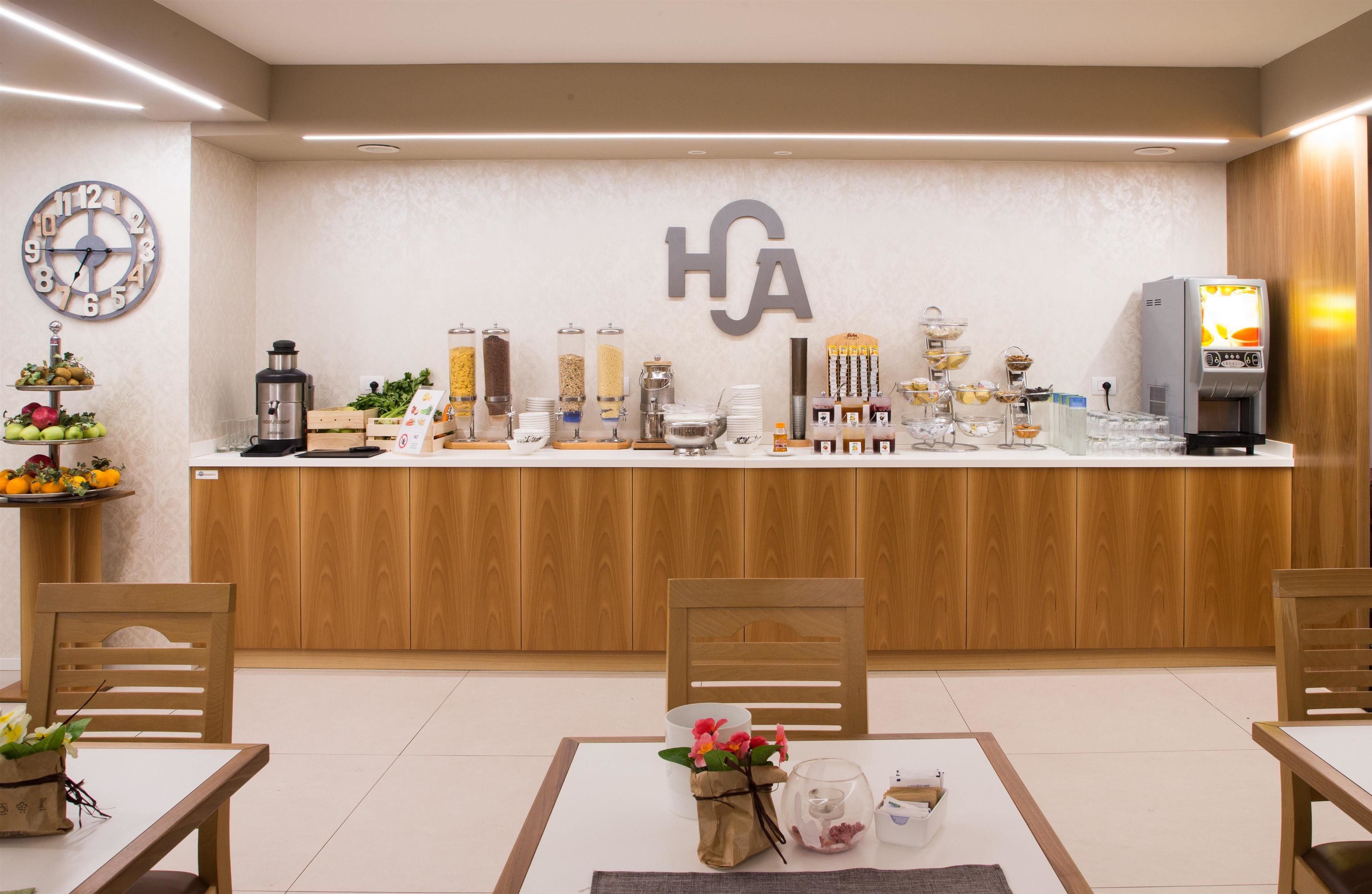 Un espace d’accueil d’hôtel avec un comptoir en bois, une horloge et divers équipements, comme une machine à café et un réfrigérateur.