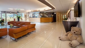 A hotel lobby with a reception desk, seating area, and a large teddy bear on the floor. - Best Western Hotel Adige (Trento)