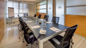 A conference room with a long table, chairs, a whiteboard, and a sign indicating the room's name.