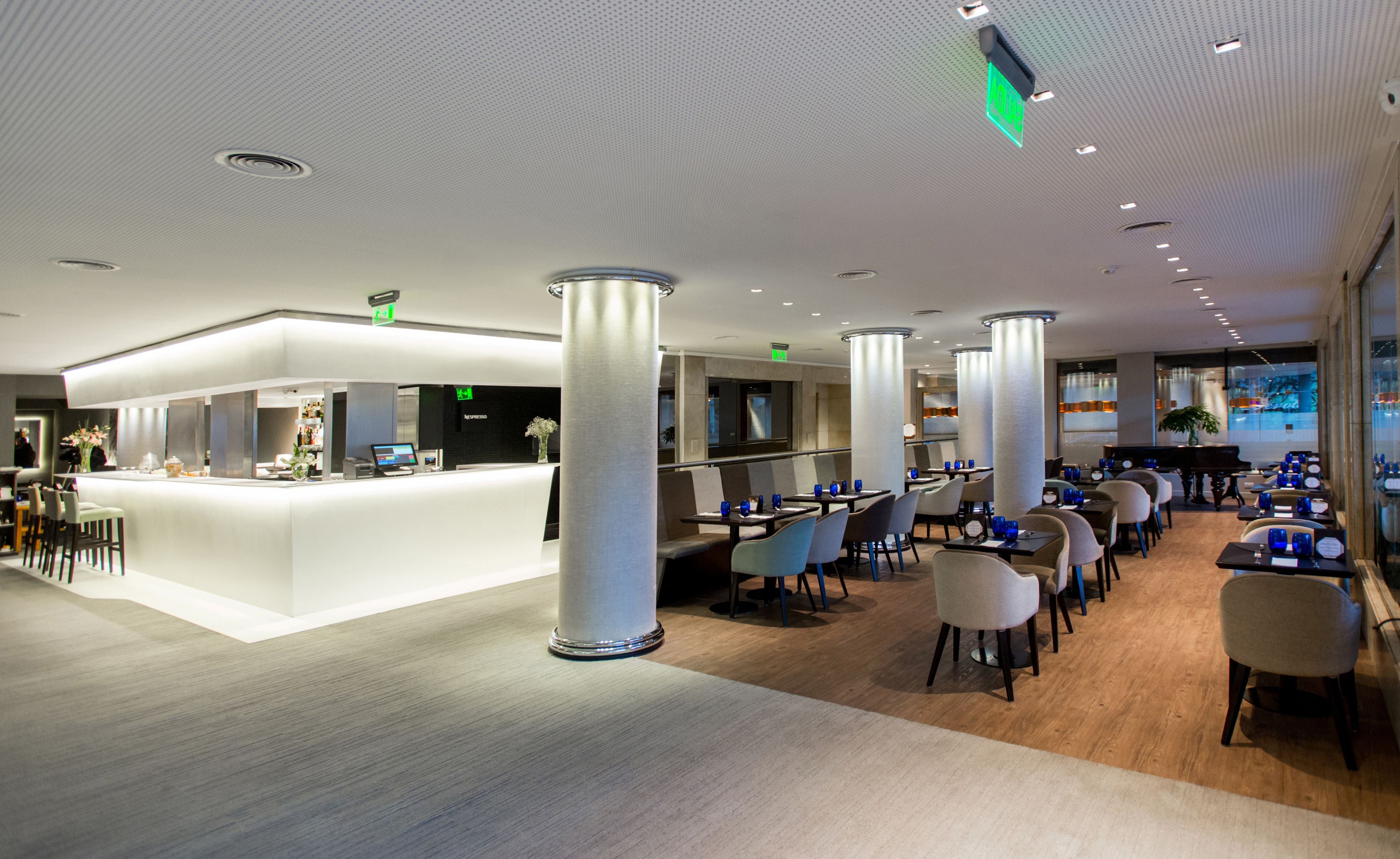 A modern restaurant with a bar area, high ceilings, and a mix of seating arrangements.