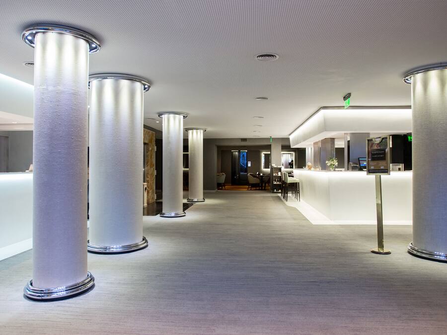 A modern hotel lobby with a central reception desk, multiple seating areas, and a high ceiling with recessed lighting.