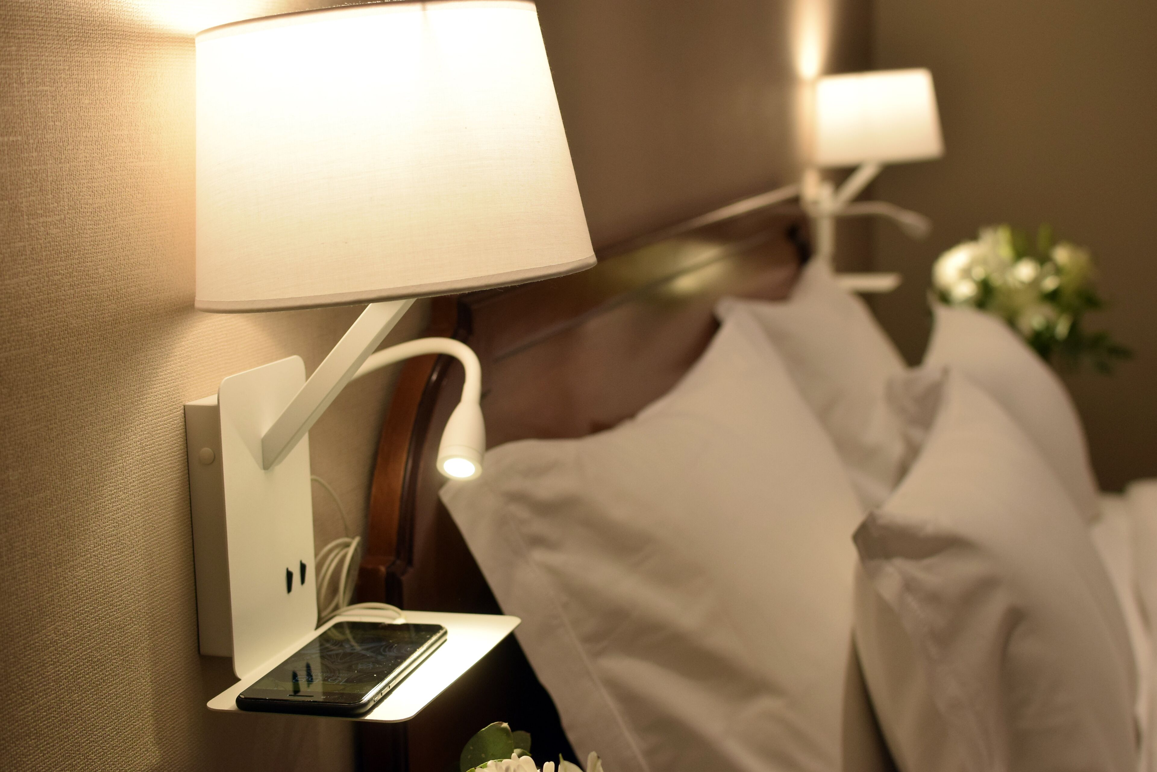 Una mesita de noche con un teléfono inteligente, una lámpara y un cargador de pared.