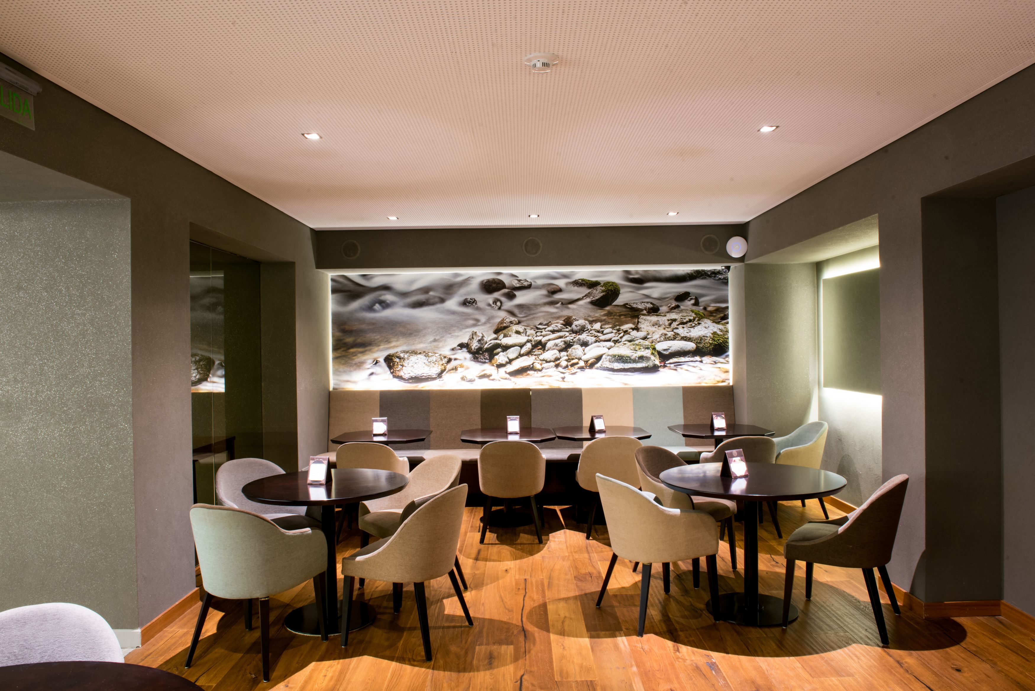 Um restaurante com mesas e cadeiras redondas, um grande mural na parede e um teto com iluminação embutida.
