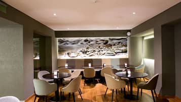 A restaurant with round tables and chairs, a large wall mural, and a ceiling with recessed lighting.