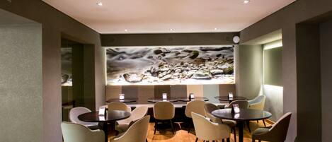 Um restaurante com mesas e cadeiras redondas, um grande mural na parede e um teto com iluminação embutida.