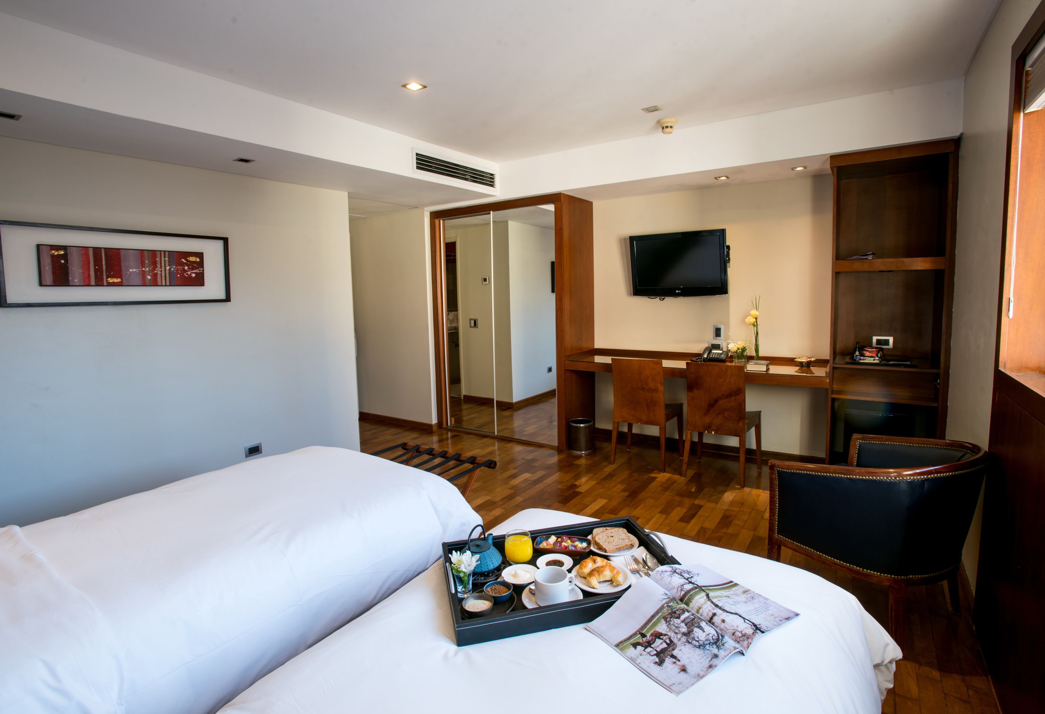 A hotel room with two beds, a desk, a chair, a TV, and a breakfast tray.
