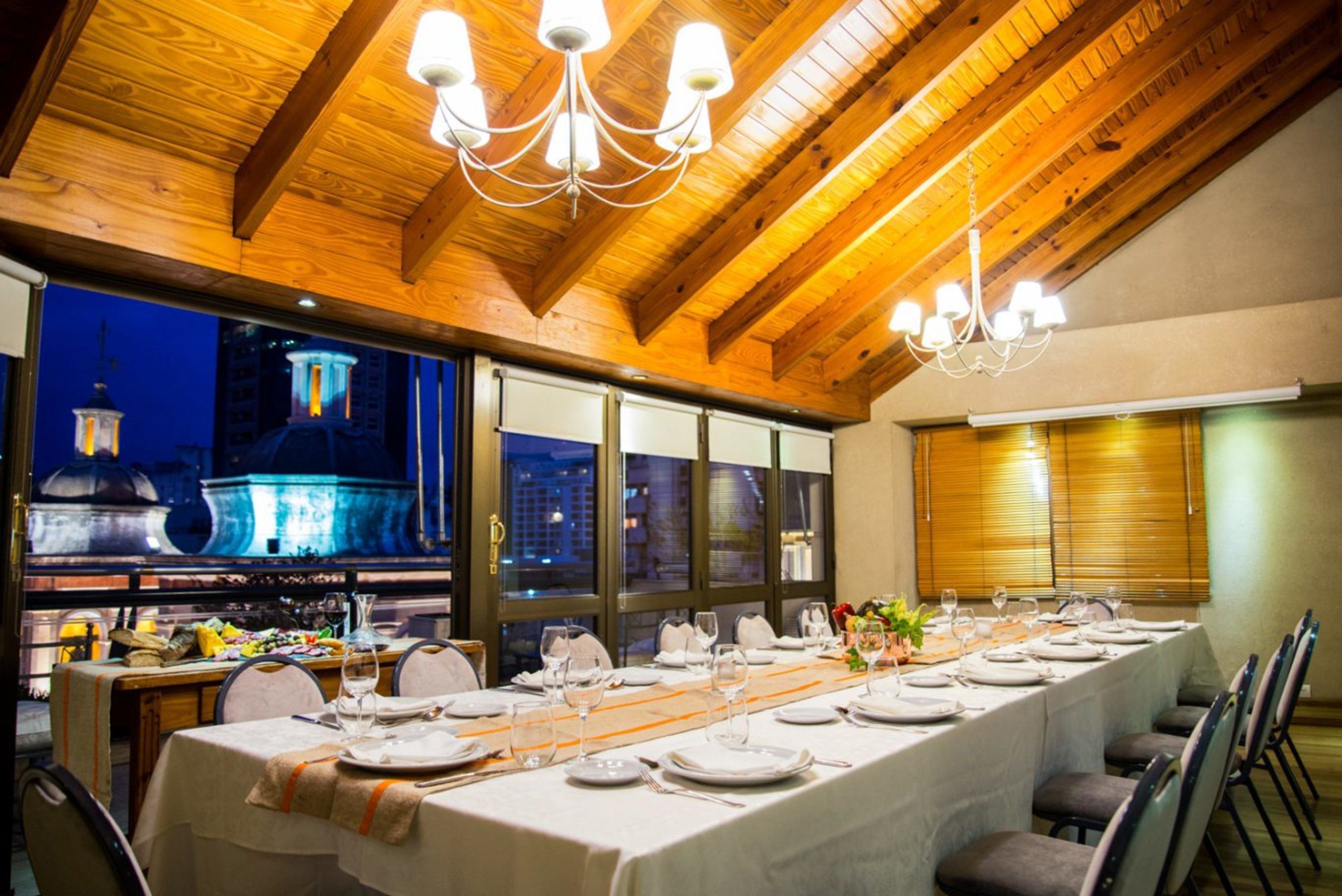 Una larga mesa de comedor dispuesta para una comida, con vista a un paisaje urbano nocturno.