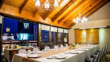 Una larga mesa de comedor dispuesta para una comida, con vista a un paisaje urbano nocturno.