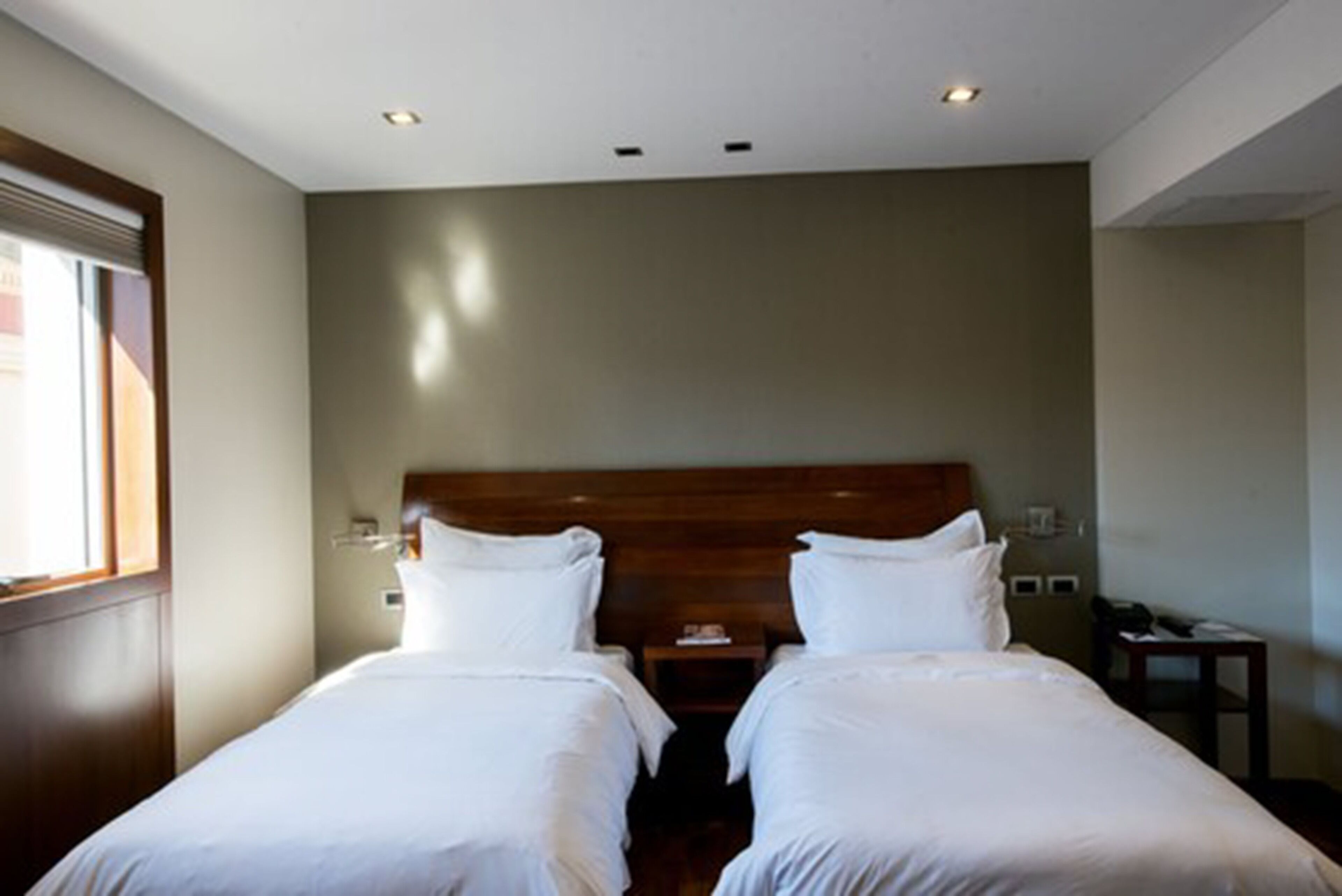 A hotel room with two single beds, a wooden headboard, a nightstand, and a small table.