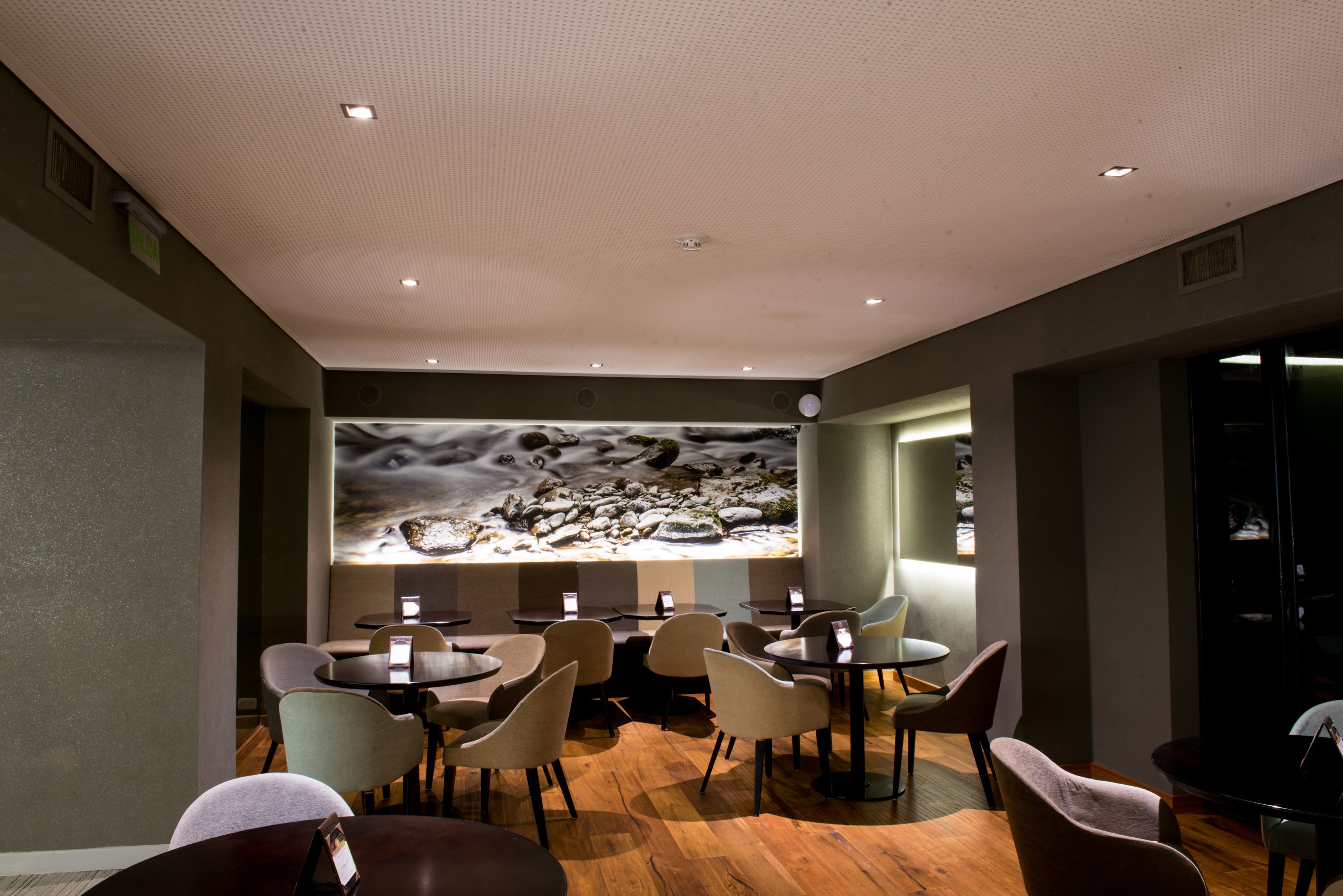 Un restaurante moderno con mesas y sillas redondas, un mural grande en la pared e iluminación empotrada en el techo.