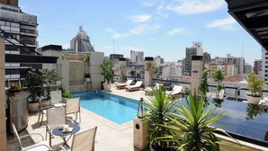 A rooftop pool area with lounge chairs and a dining table, surrounded by potted plants and overlooking a cityscape. - Windsor Hotel And Tower (Córdoba)