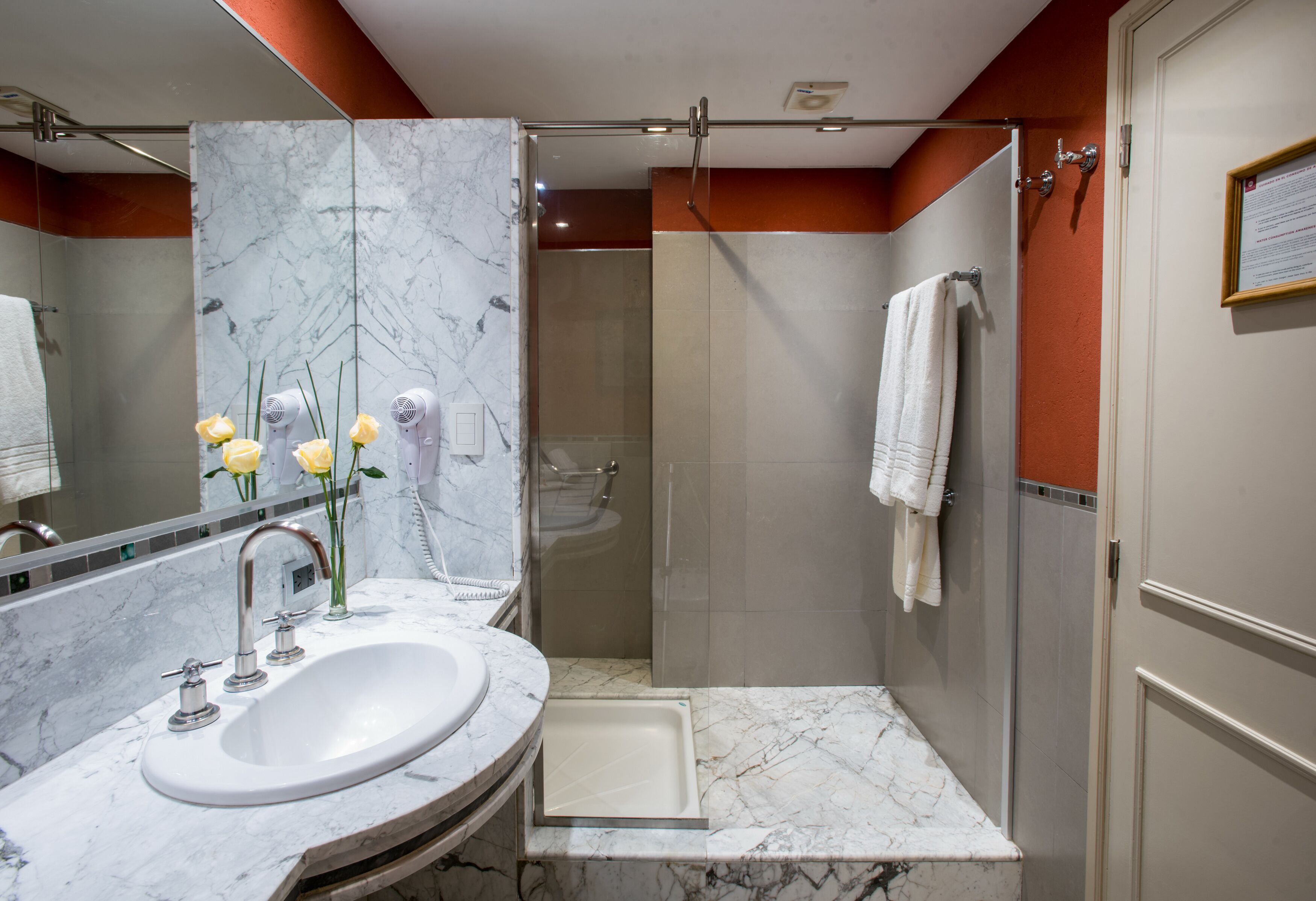 Un baño con lavamanos de mármol, ducha con mampara de vidrio y un perchero para toallas.