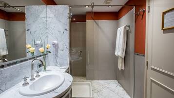 Un baño con lavamanos de mármol, ducha con mampara de vidrio y un perchero para toallas.