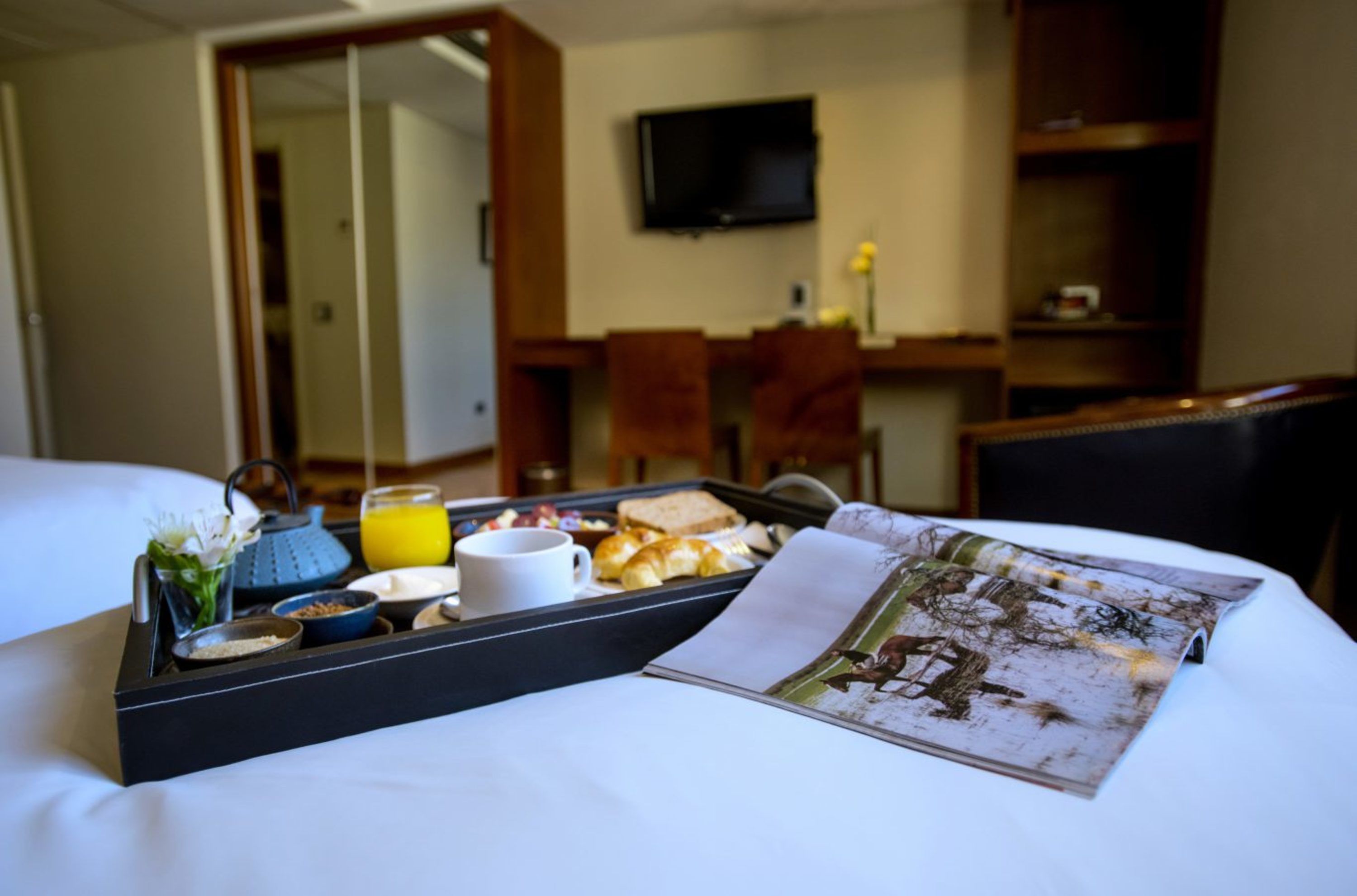 Habitación de hotel con cama, una bandeja con alimentos para el desayuno, televisión y escritorio.