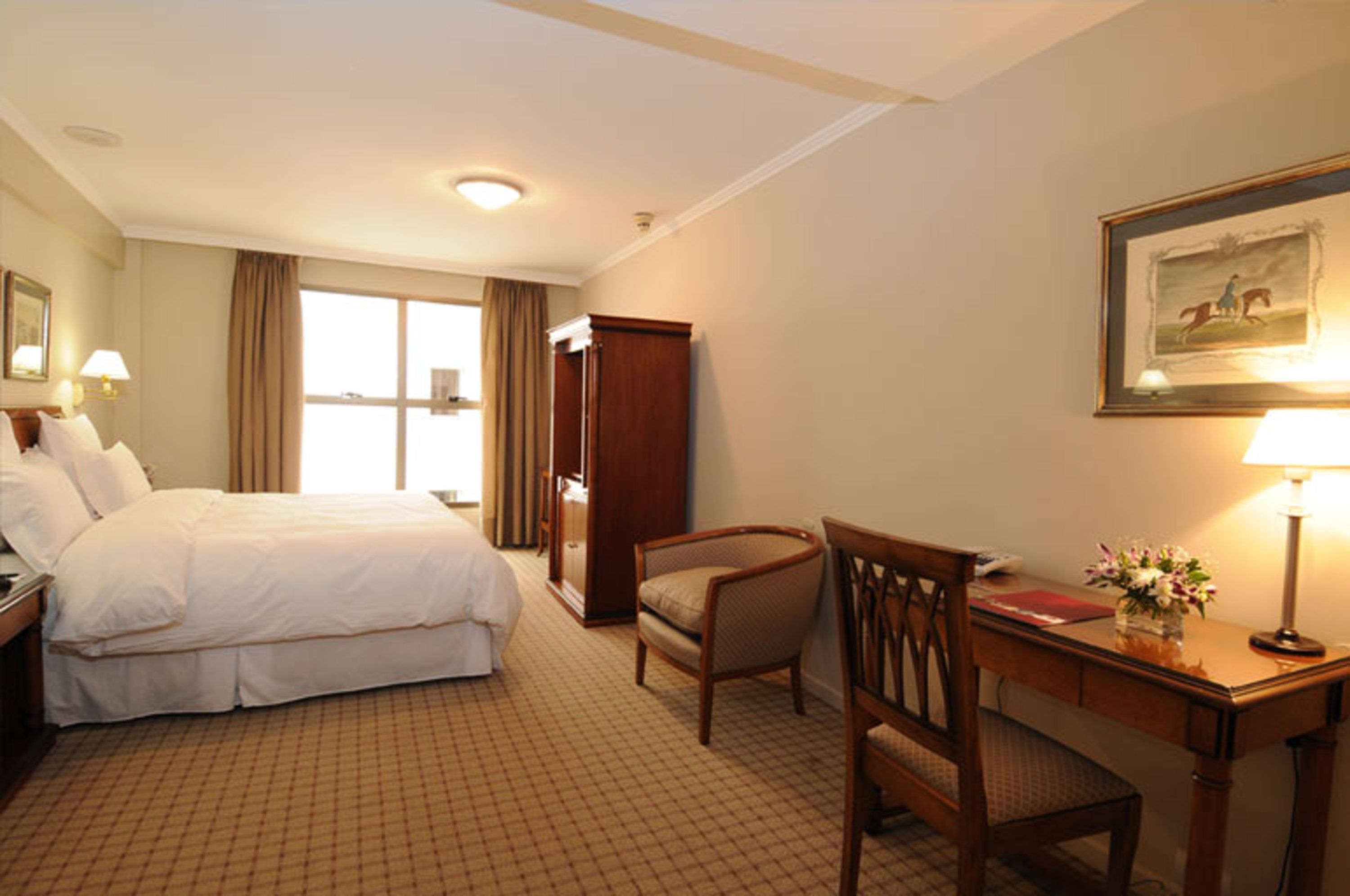 Une chambre d’hôtel avec un grand lit, un bureau avec une lampe, une chaise et un tableau encadré au mur.